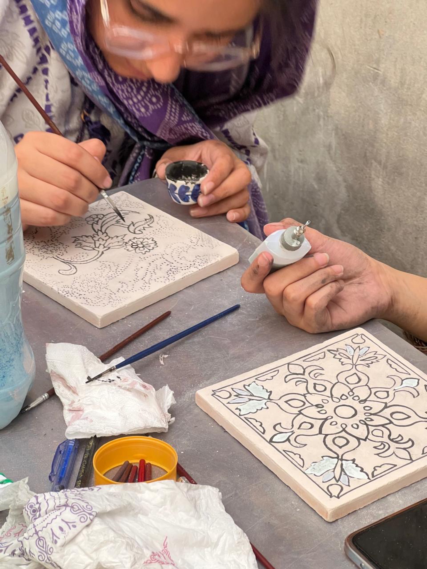 Kashi Kari hands-on practice with Kashi Kari Experts Amjad Daudpota, Taimoor Daudpota and Arsalan Daudpota — brush painting traditional Sozenkari patterns on tiles.